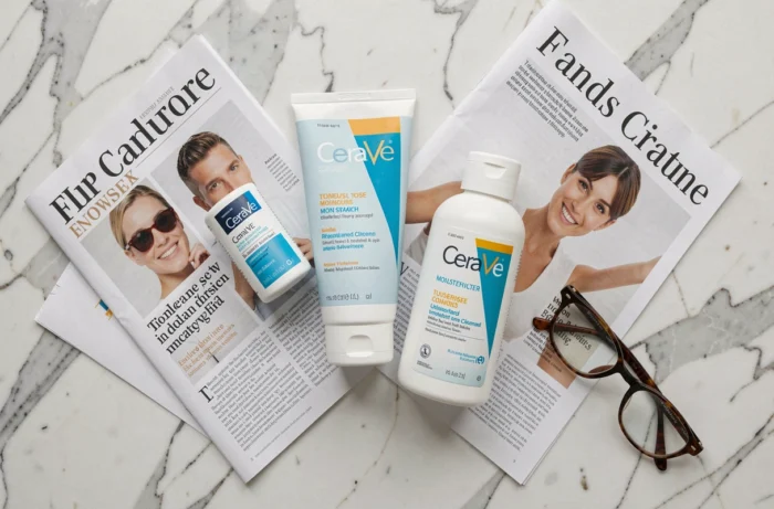 Plat posé de produits CeraVe sur marbre avec articles de presse, illustration du débat sur l'appartenance de la marque à L'Oréal
